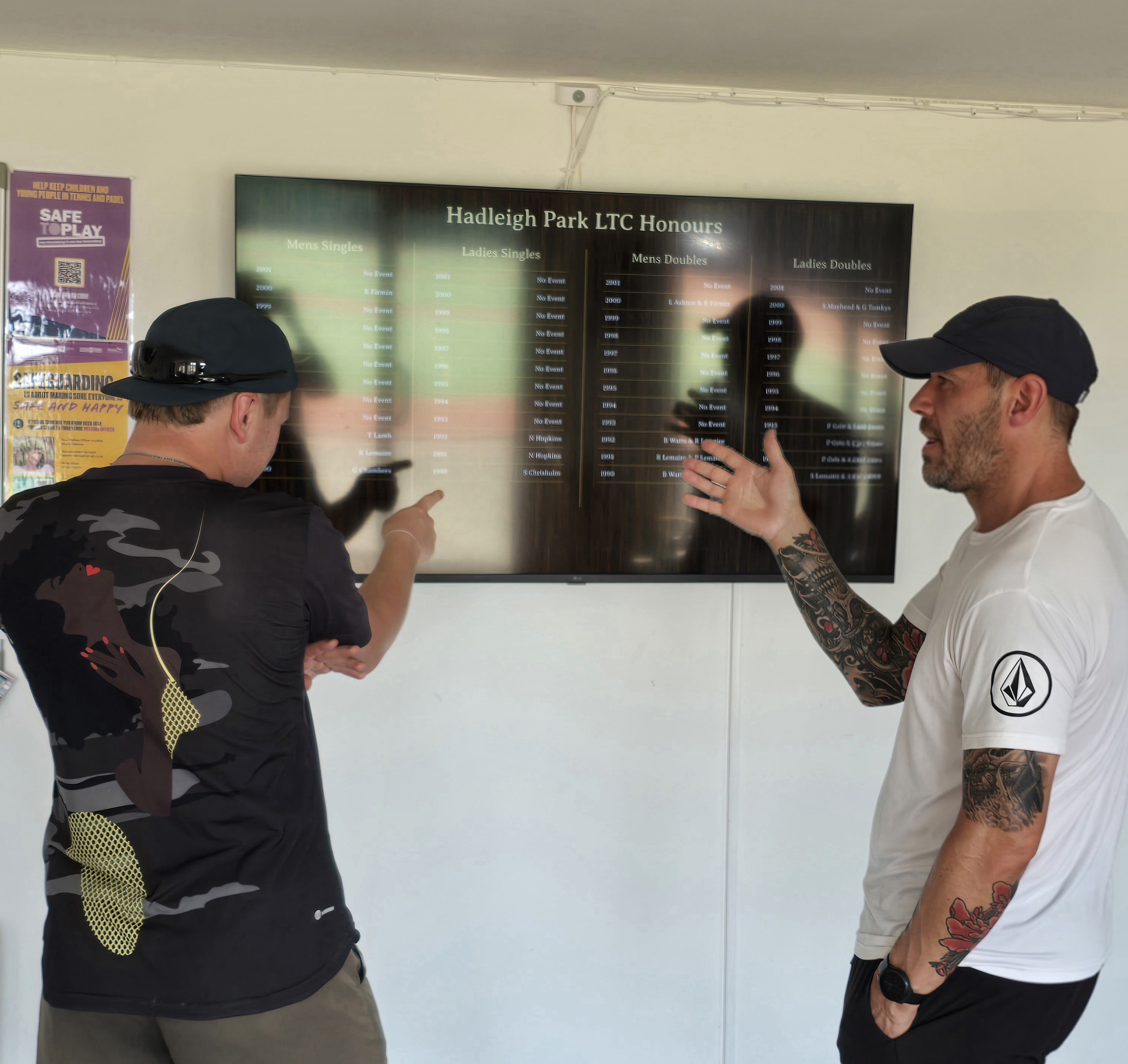 Honours board visible above a bar with staff standing below in a busy social club environment